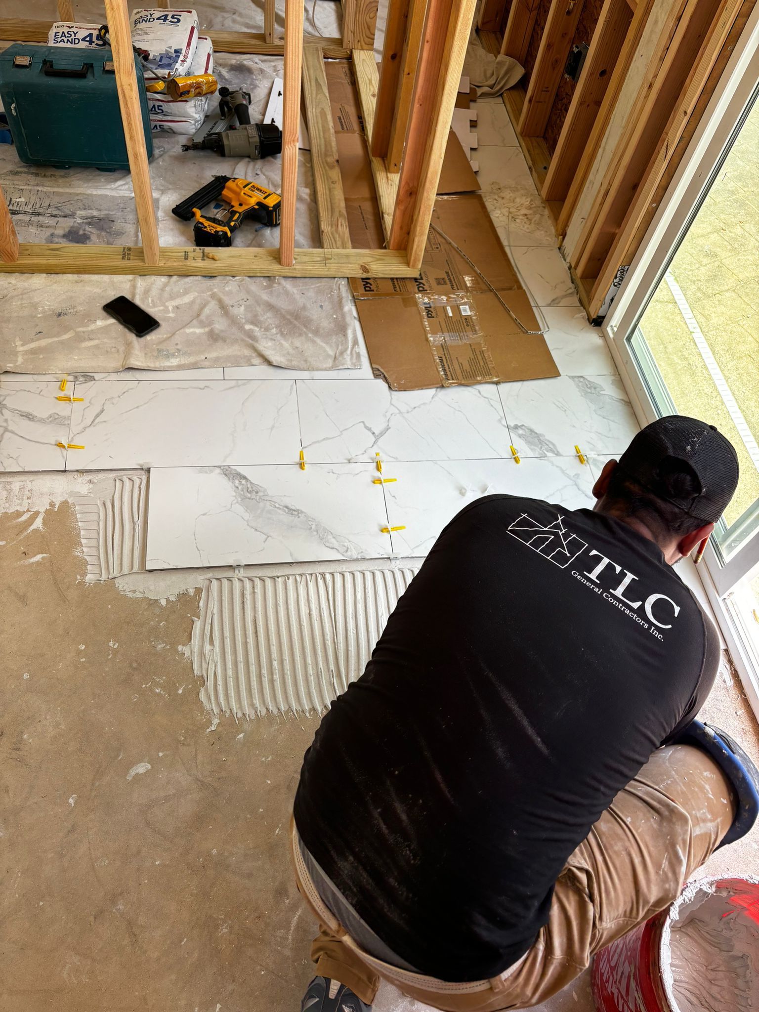 A man is kneeling down in a room while laying tile on the floor.