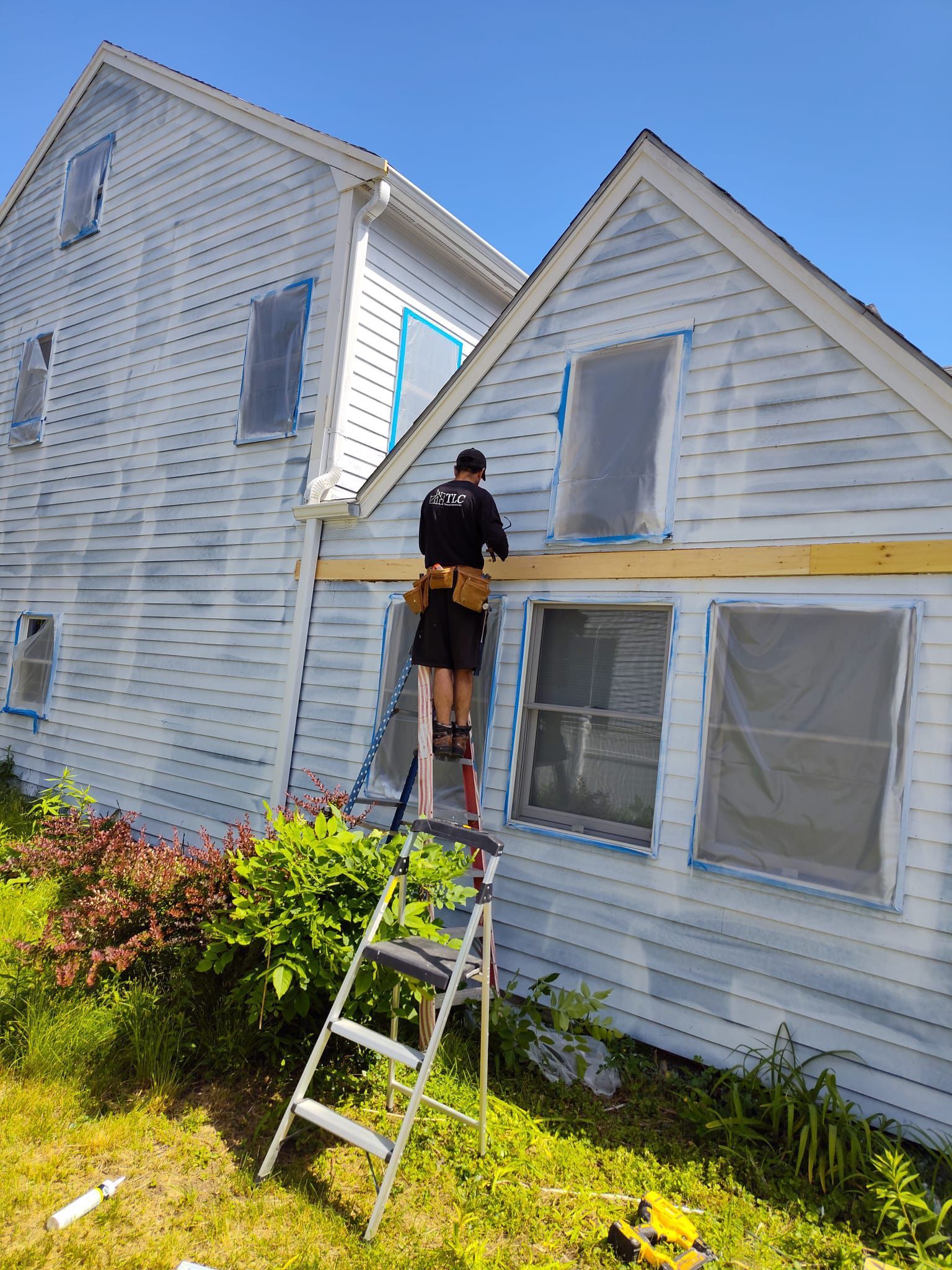A man is standing on a ladder painting a white house.