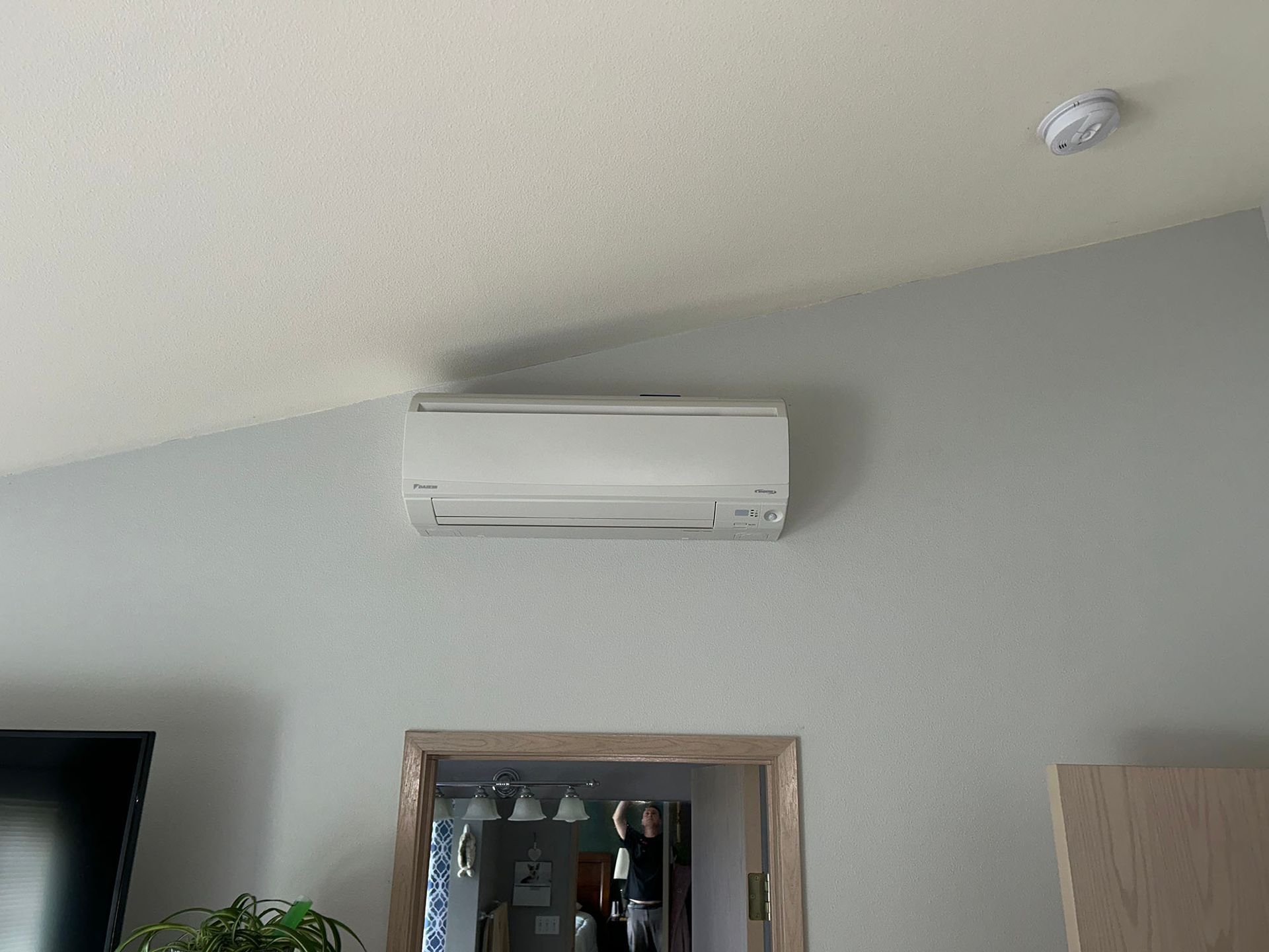 A white air conditioner is hanging from the ceiling in a living room.