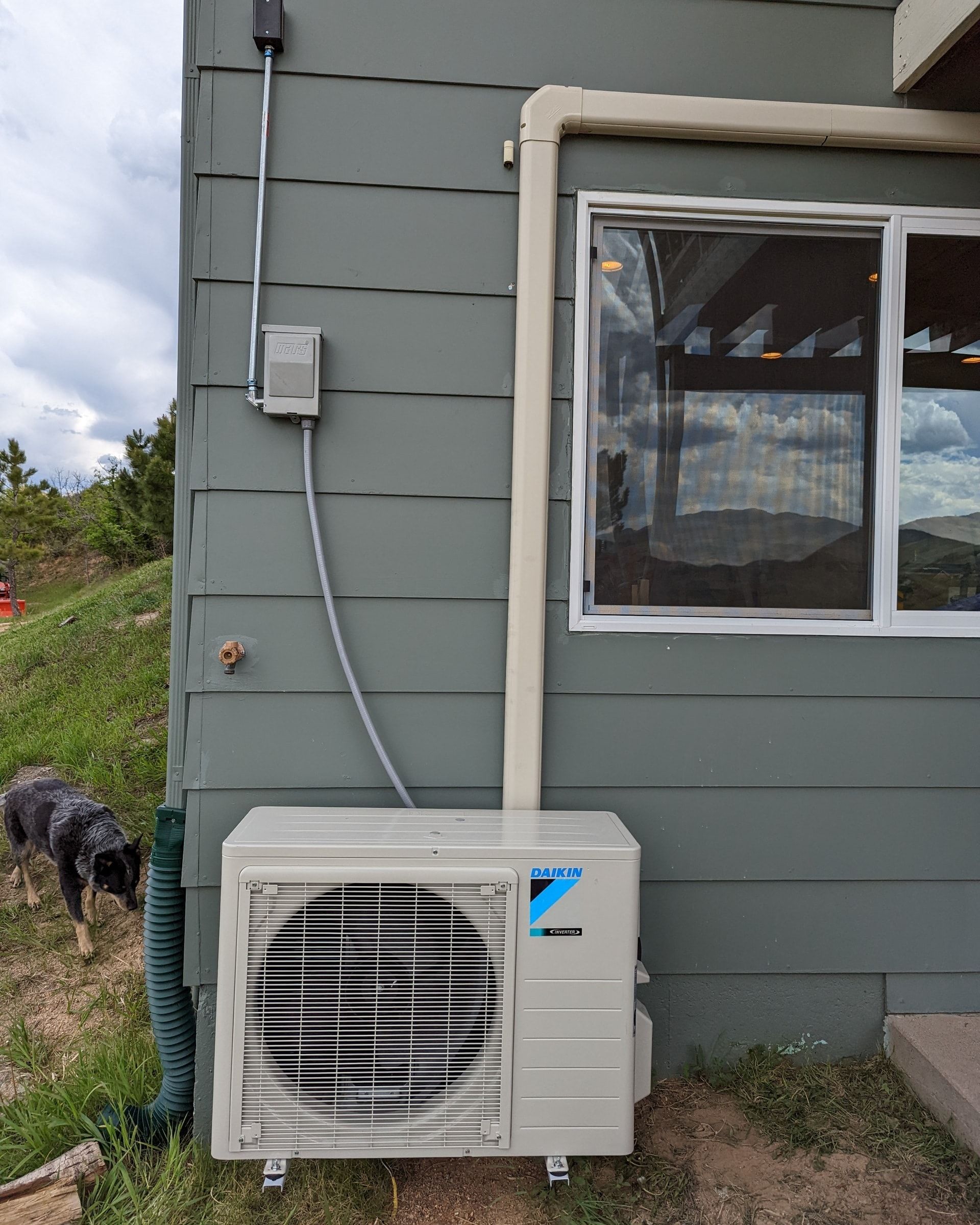 A white air conditioner is mounted on the side of a house next to a window.