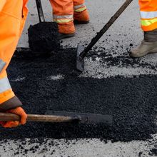 A man is using a shovel to spread asphalt on the ground.