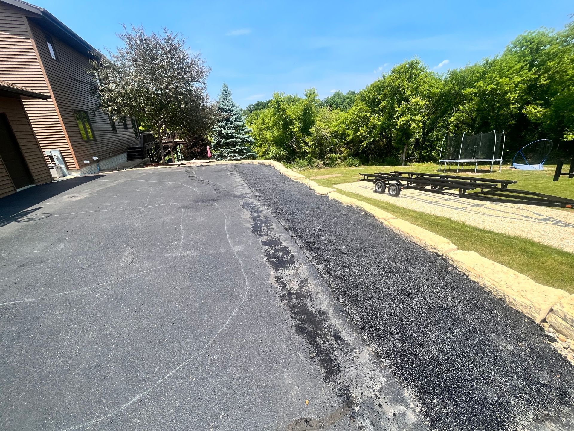 A road with a picnic table on the side of it and a house in the background.