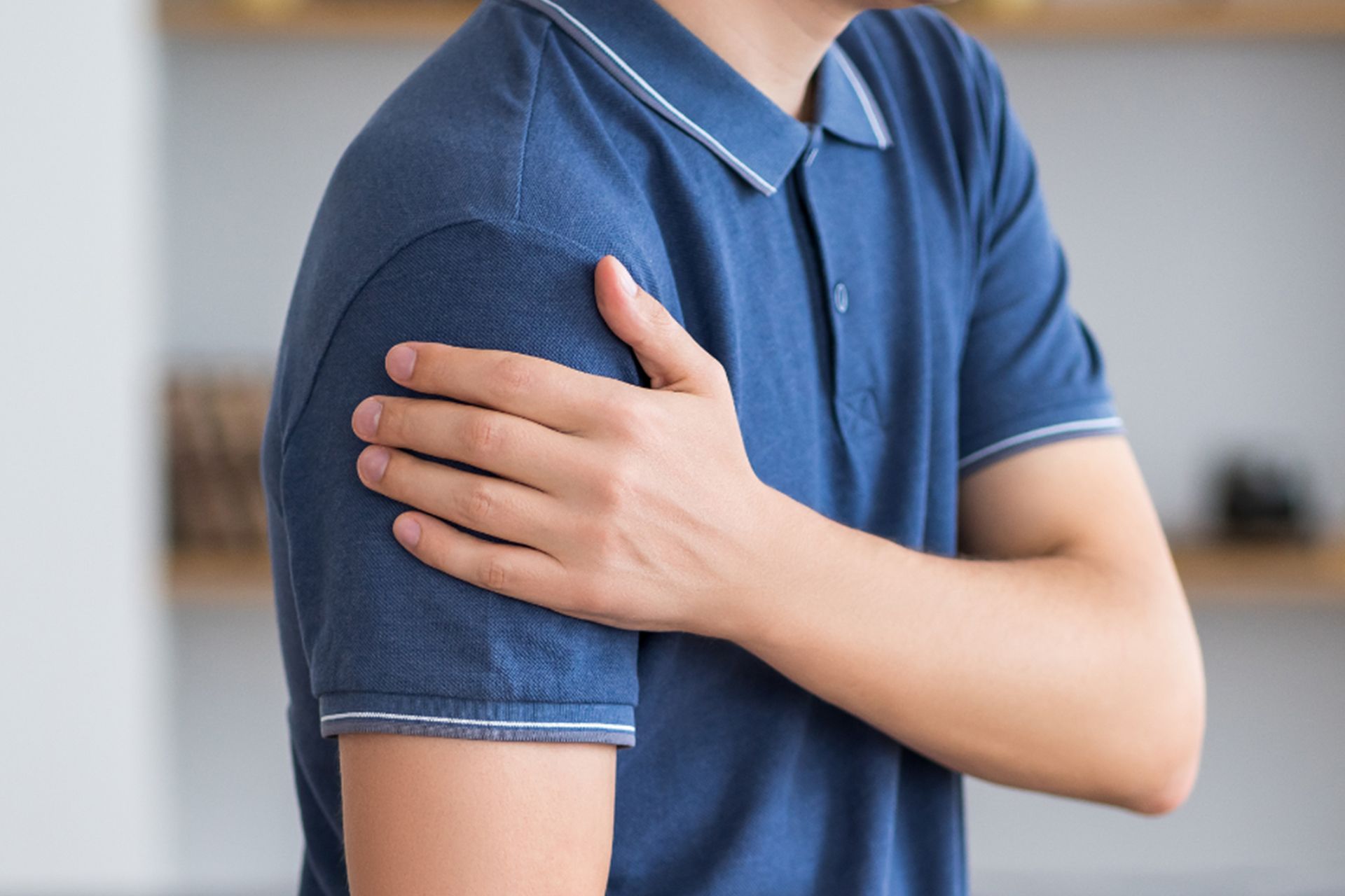 A man in a blue shirt is holding his shoulder in pain.