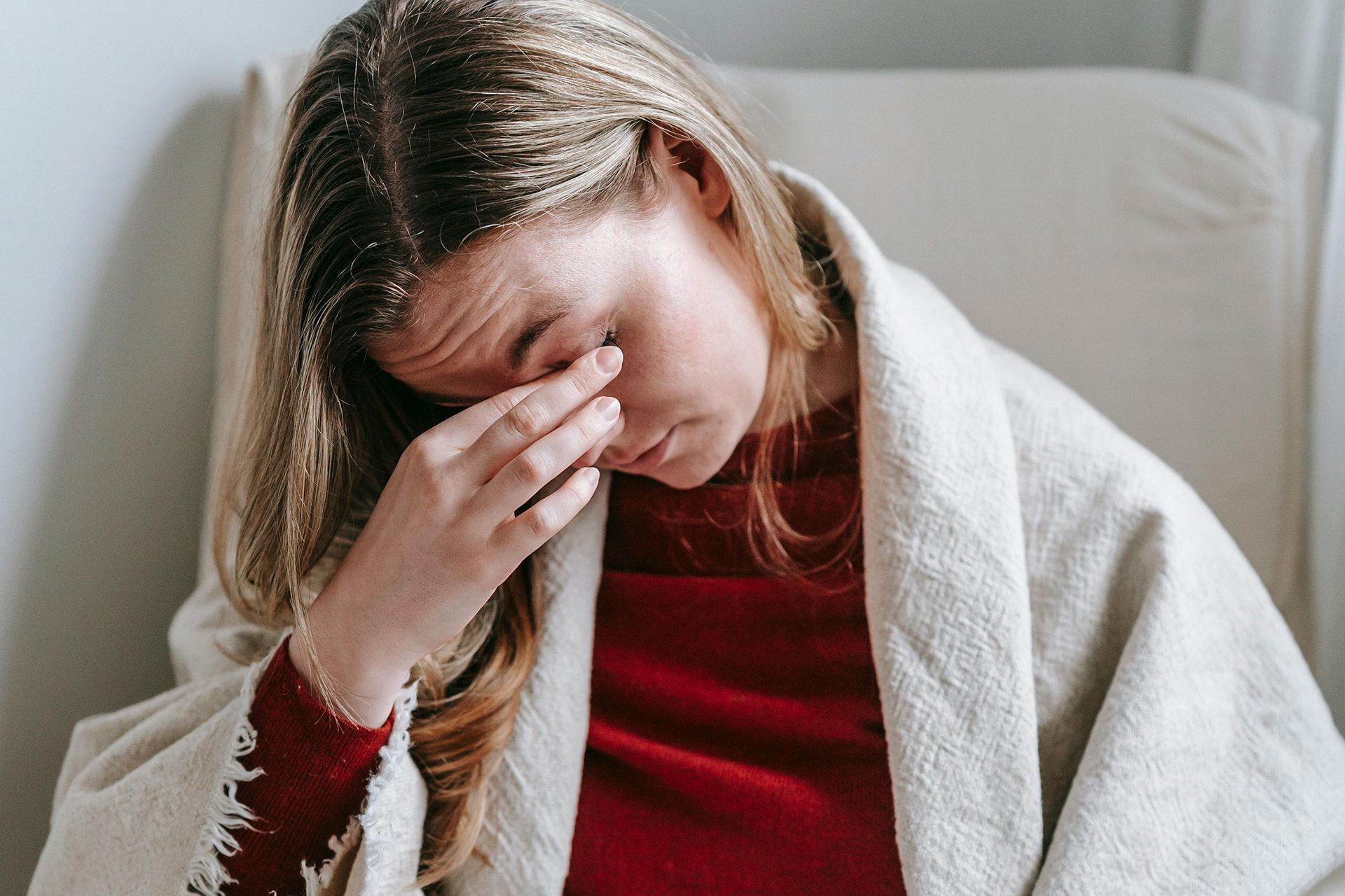 A woman wrapped in a blanket is sitting in a chair holding her head.