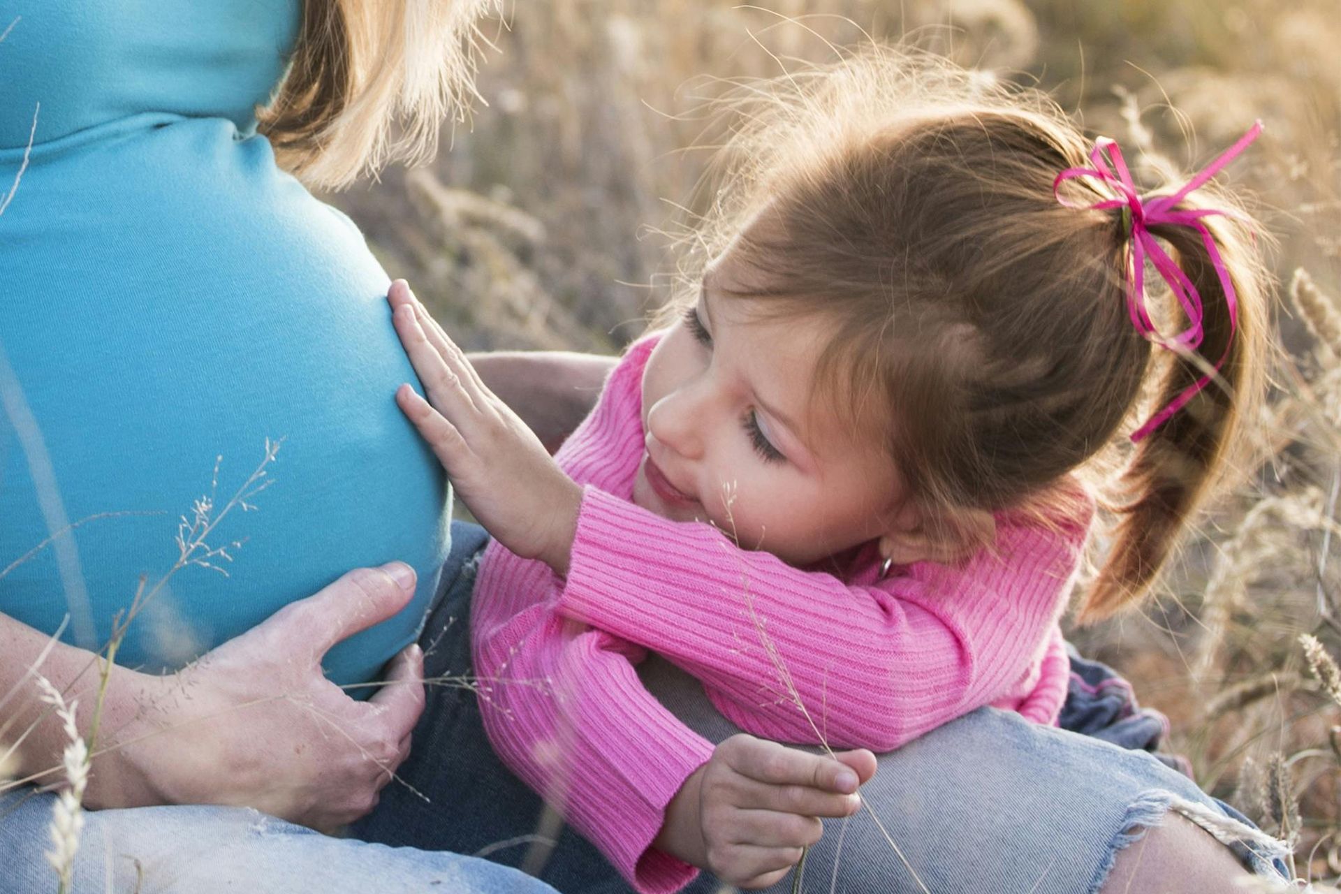 A little girl is hugging a pregnant woman's belly.