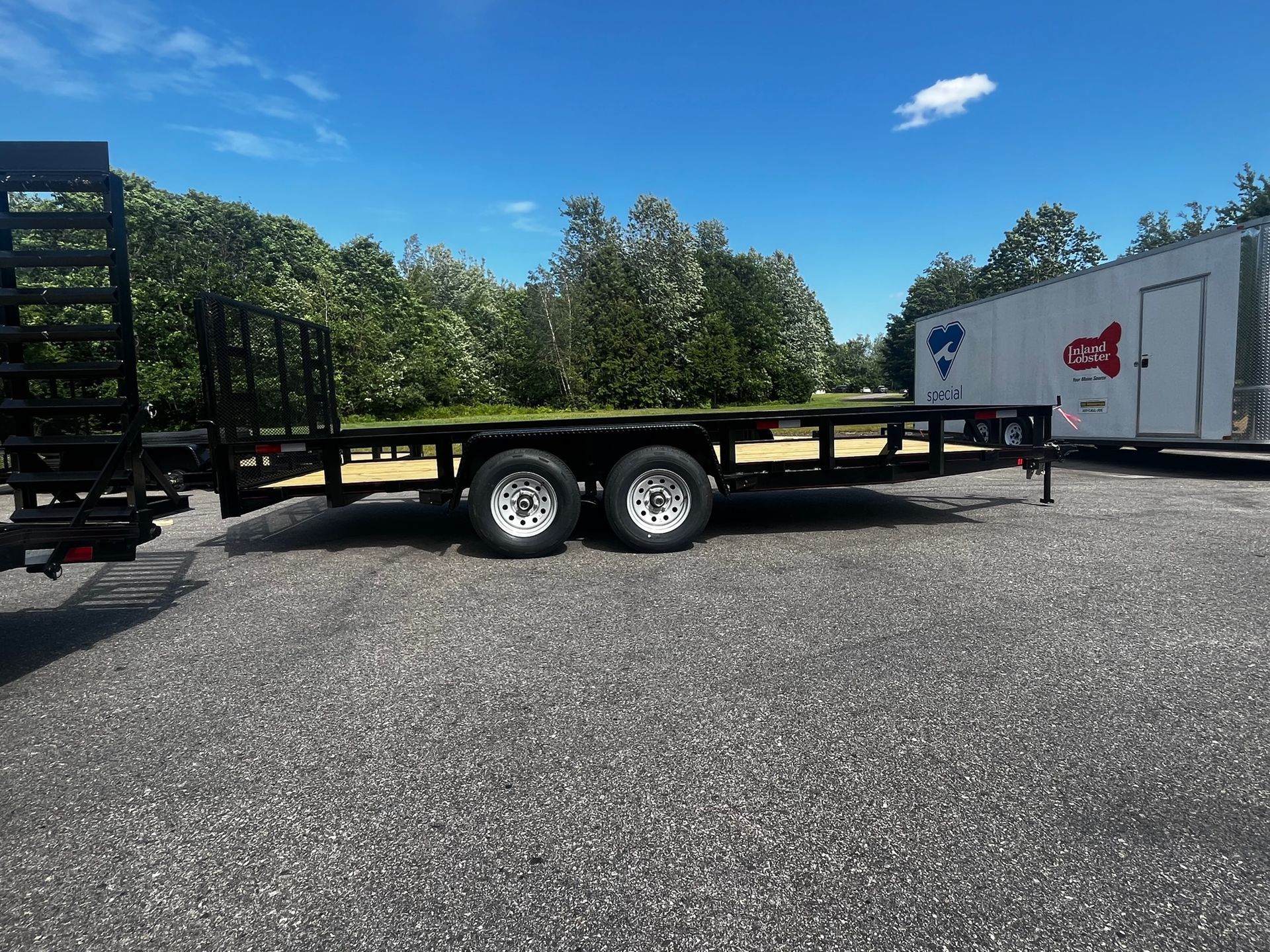 A trailer is parked in a gravel lot next to a white trailer.