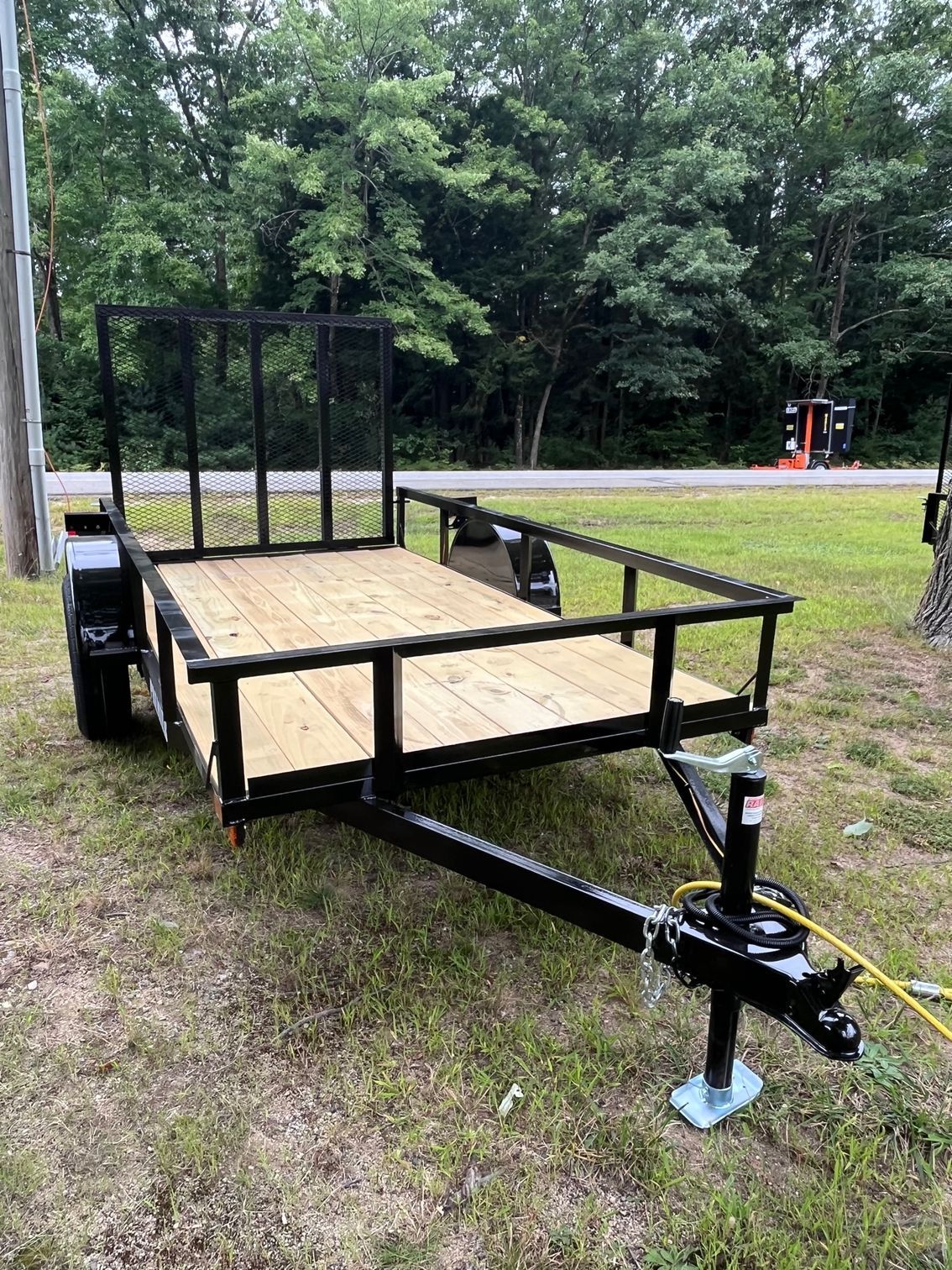 A small trailer is parked in the grass next to a road.