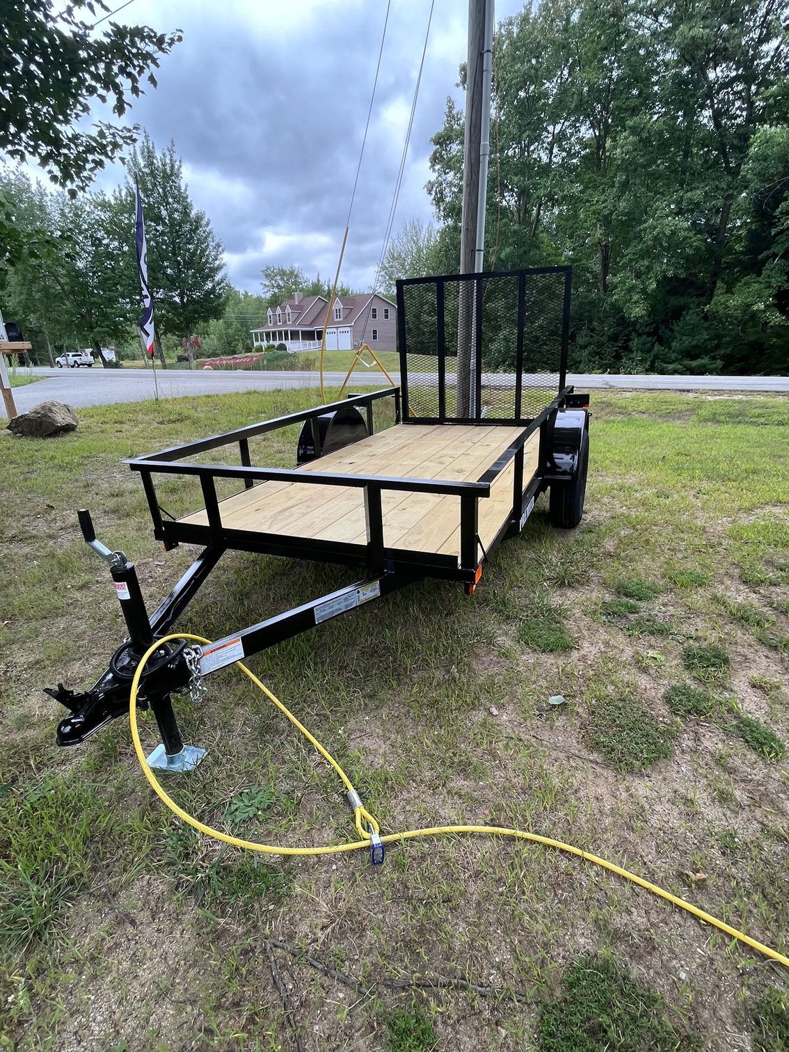 A small trailer is parked in a grassy field next to a road.