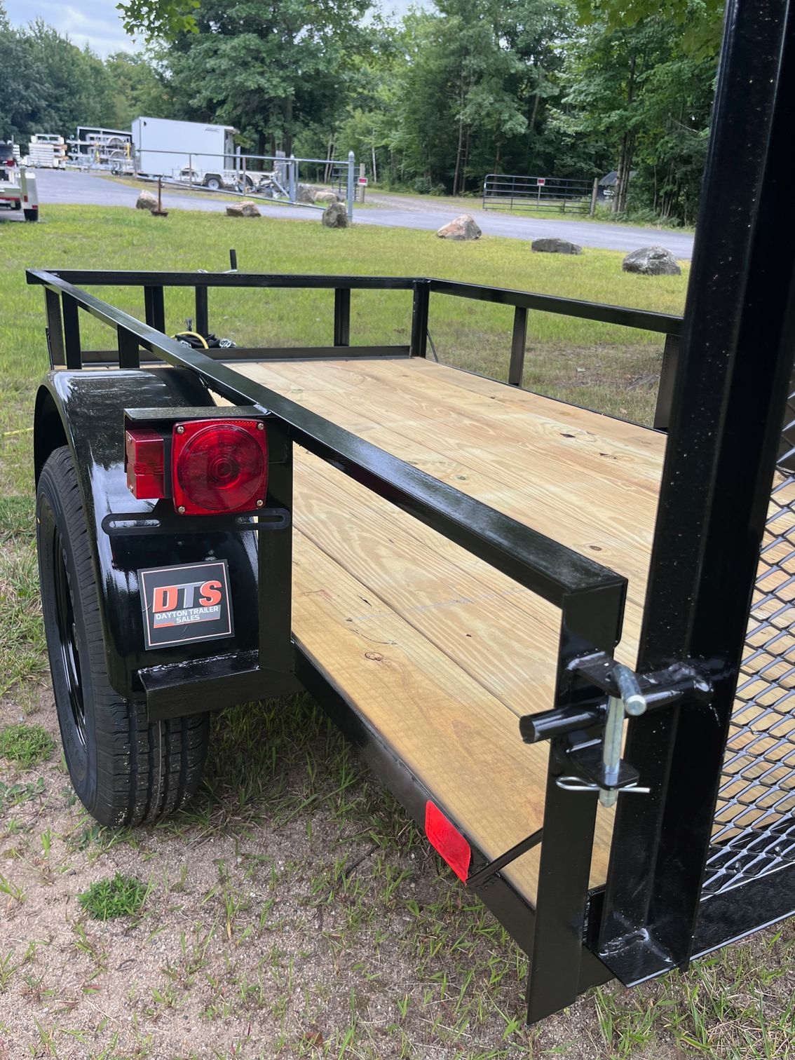 A trailer with a wooden deck is parked in the grass.