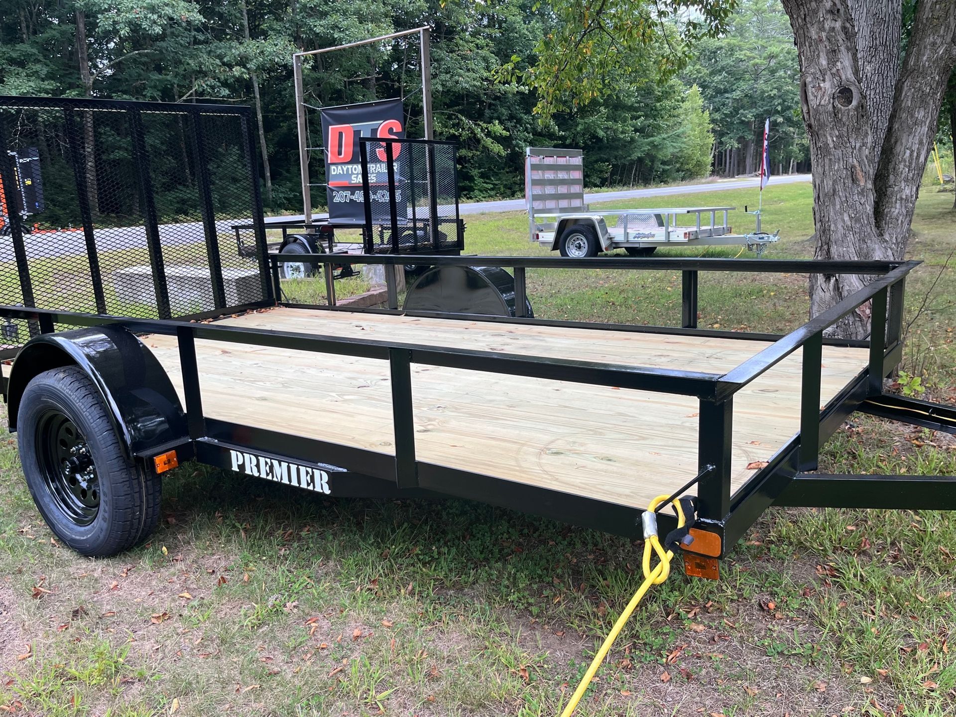 A trailer is parked in the grass next to a tree.