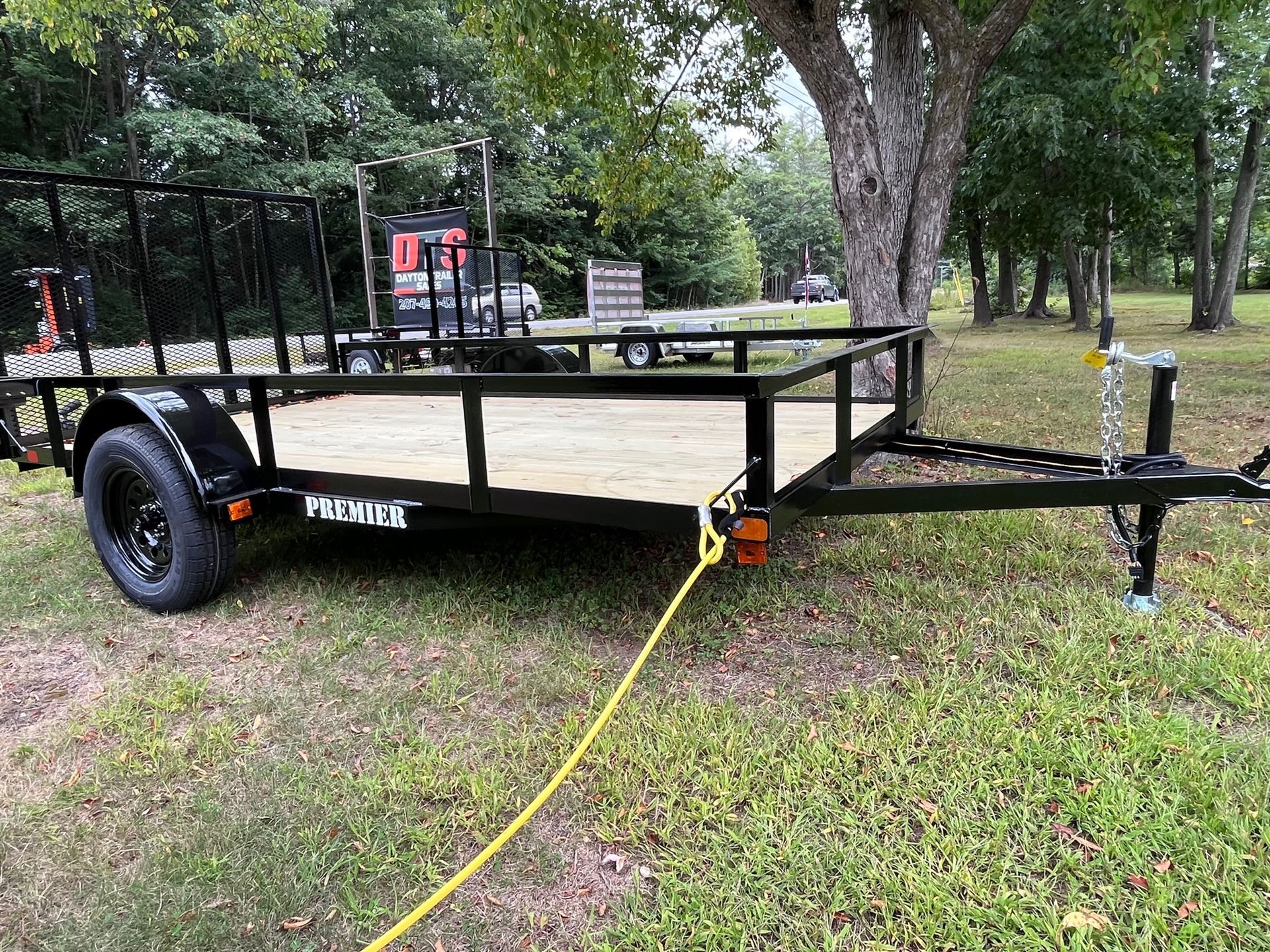 A trailer is parked in the grass next to a tree.
