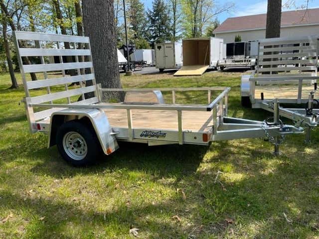 A small trailer is parked in the grass next to a tree.
