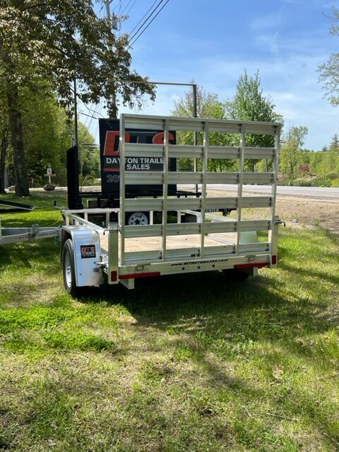 A trailer with a fence on the back is parked in the grass.