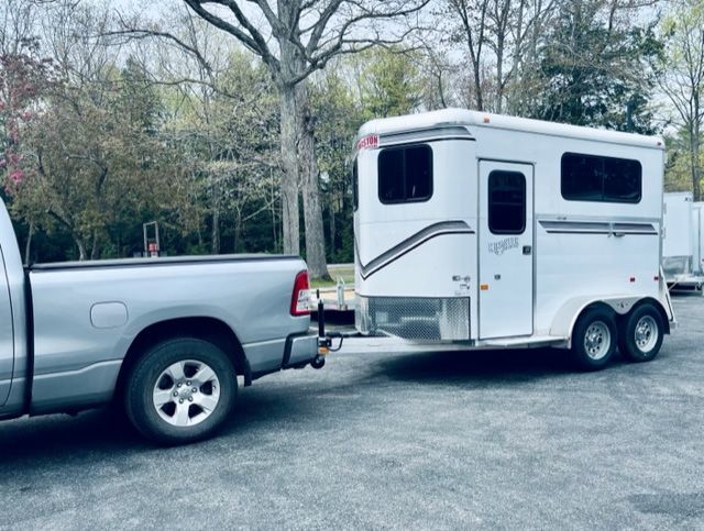 A silver truck is towing a white horse trailer.