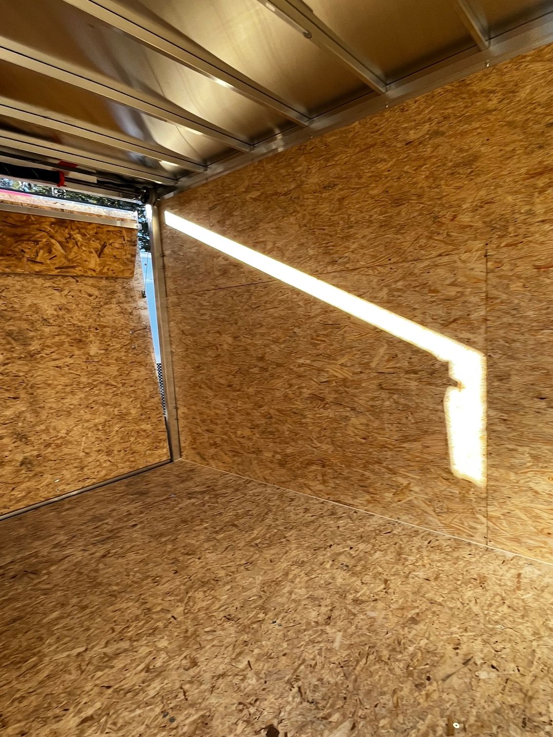 A room with a wooden wall and a light coming through the door.