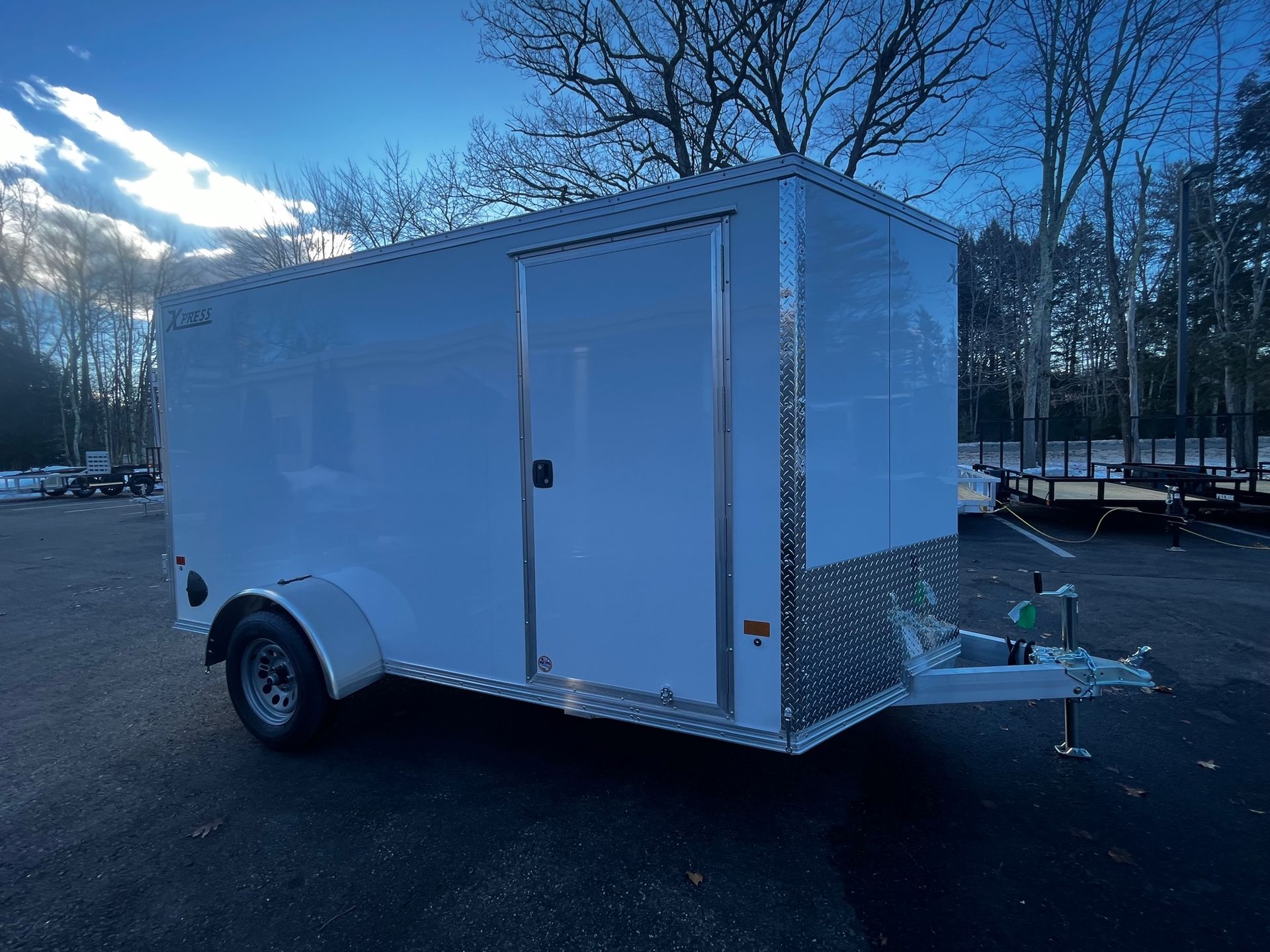 A white trailer is parked in a parking lot with trees in the background