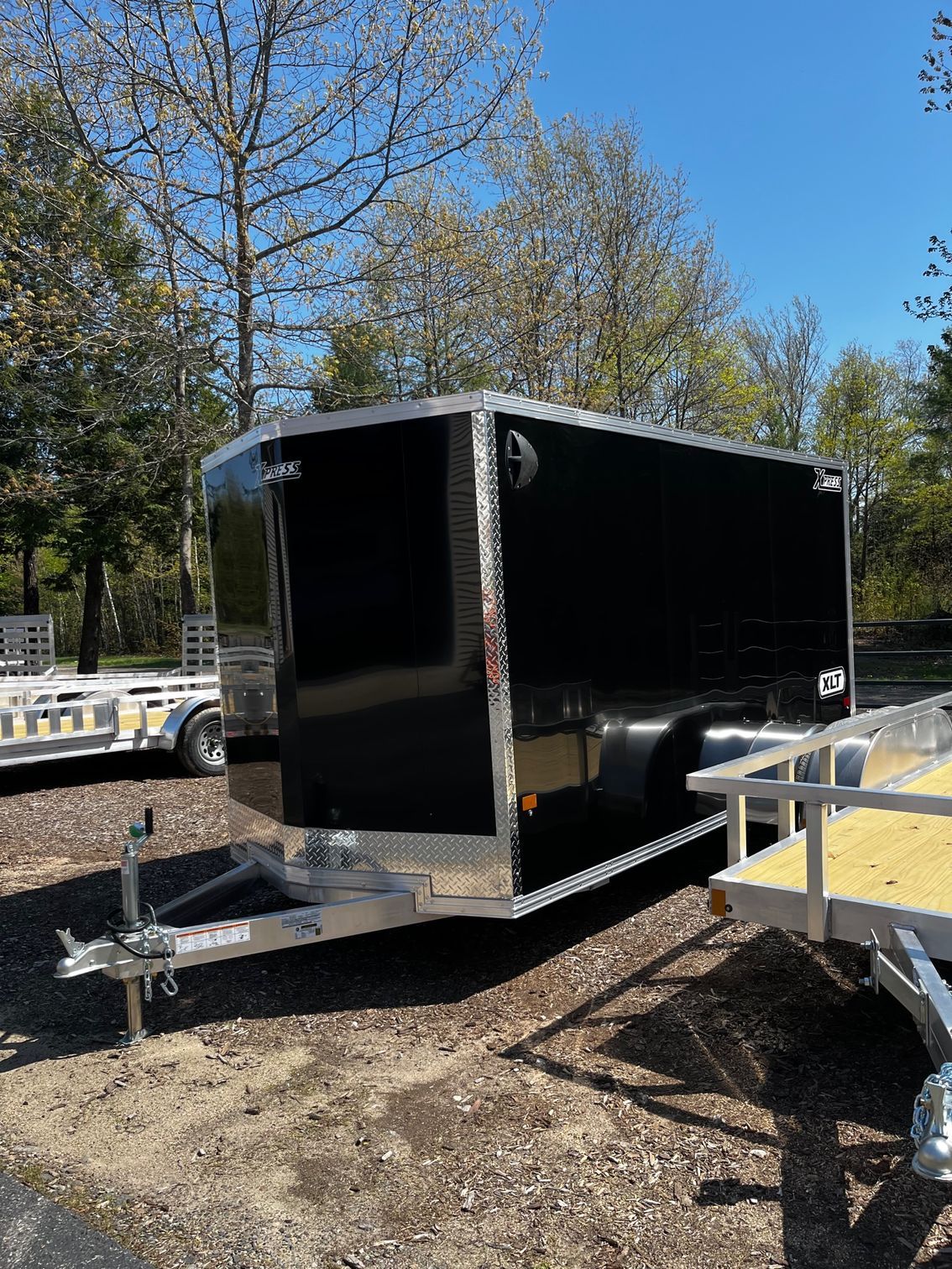 A black trailer is parked in a dirt lot next to a trailer.