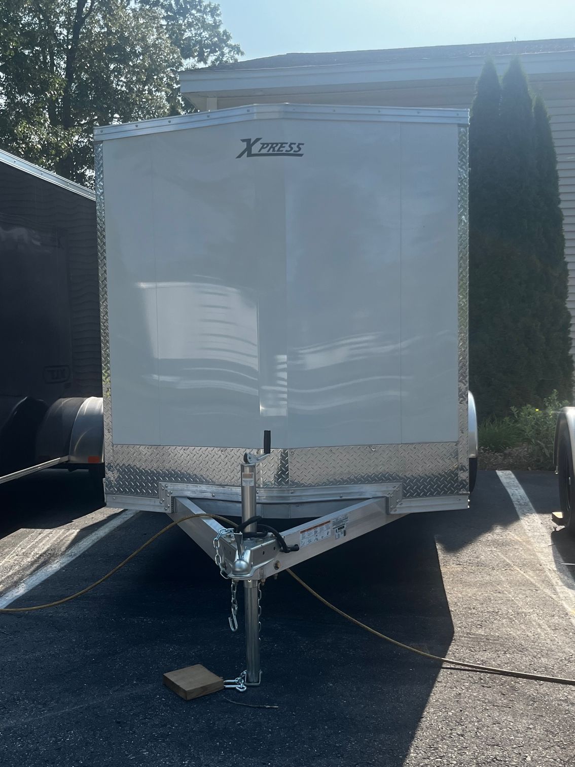 White enclosed cargo trailer parked on asphalt. Silver trim along the bottom and tongue, with a logo at the top.