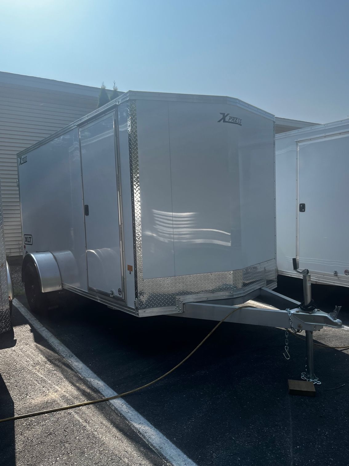 A white enclosed cargo trailer with a silver diamond plate trim is parked outside under a sunny sky.