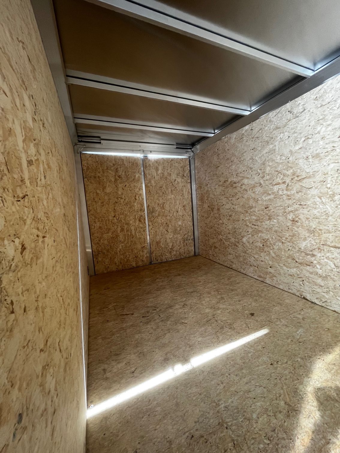 Interior of an empty cargo trailer. The walls, ceiling, and floor are made of light-colored wood.