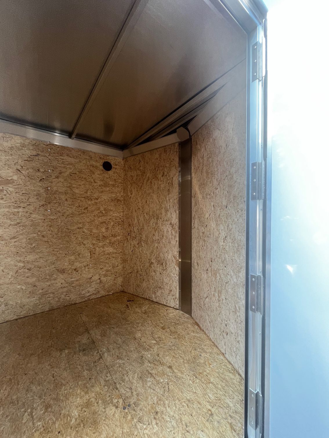 Interior view of an empty trailer, with exposed wood walls and metal supports. The door frame and hinges are visible on the right side.
