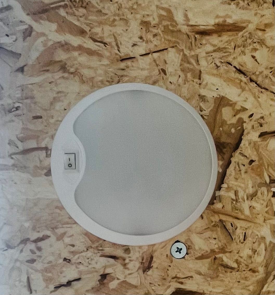 White, round ceiling light with an on/off switch, mounted on a wood-chip textured wall.