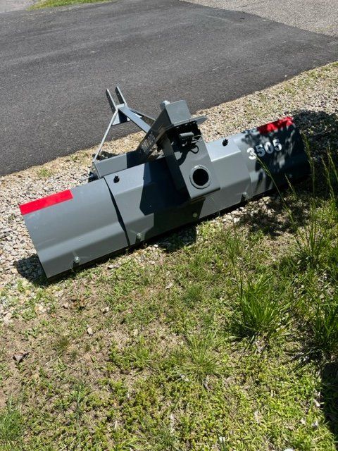 A large gray object is sitting in the grass next to a road.