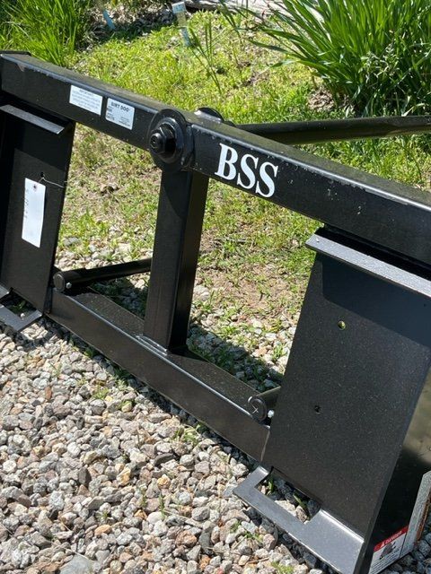 A bss forklift attachment is sitting on a gravel road.