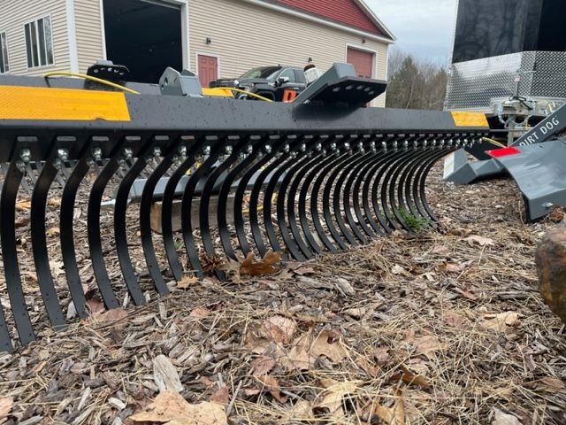 A large metal rake is sitting on top of a pile of mulch.