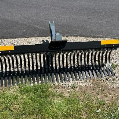 A black and yellow rake is sitting in the grass next to a road.