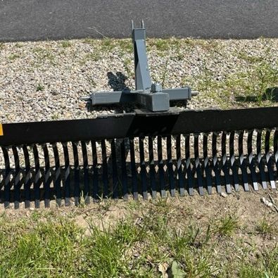 A black rake is sitting in the grass next to a gravel road.