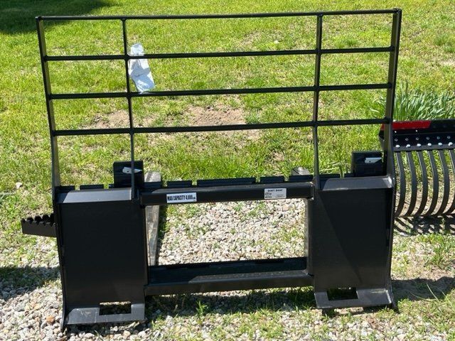 A forklift attachment is sitting in the grass next to a rake.