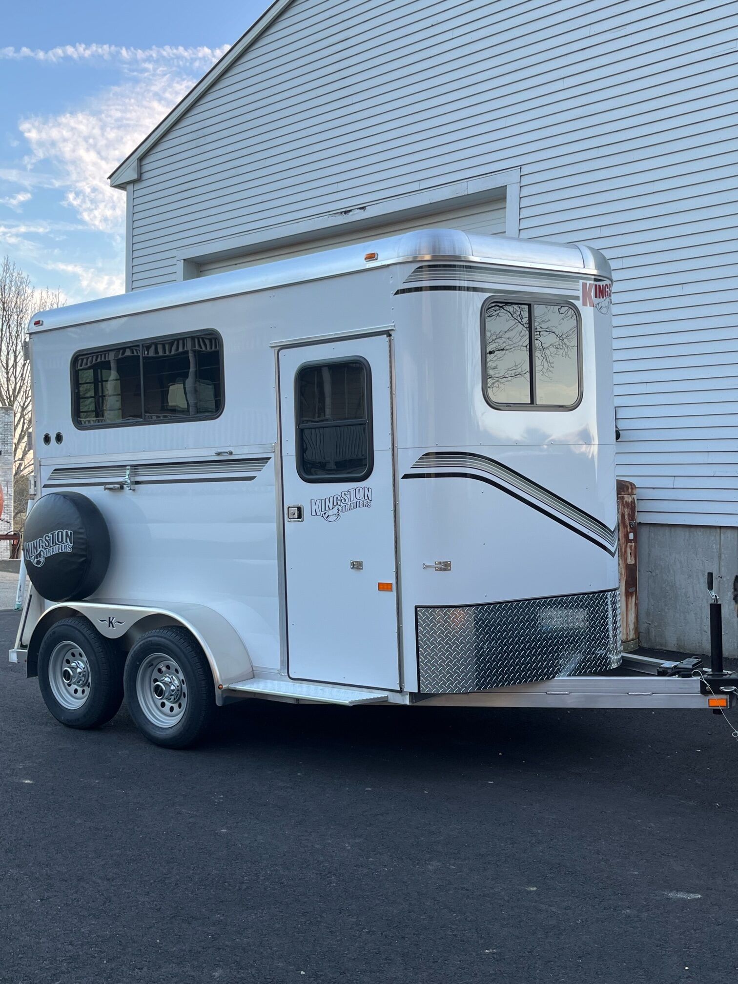 A white horse trailer is parked in front of a white house.