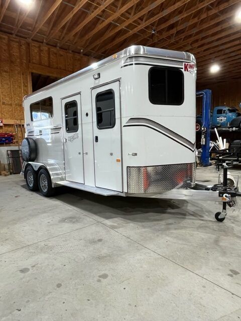 A white horse trailer is parked in a garage