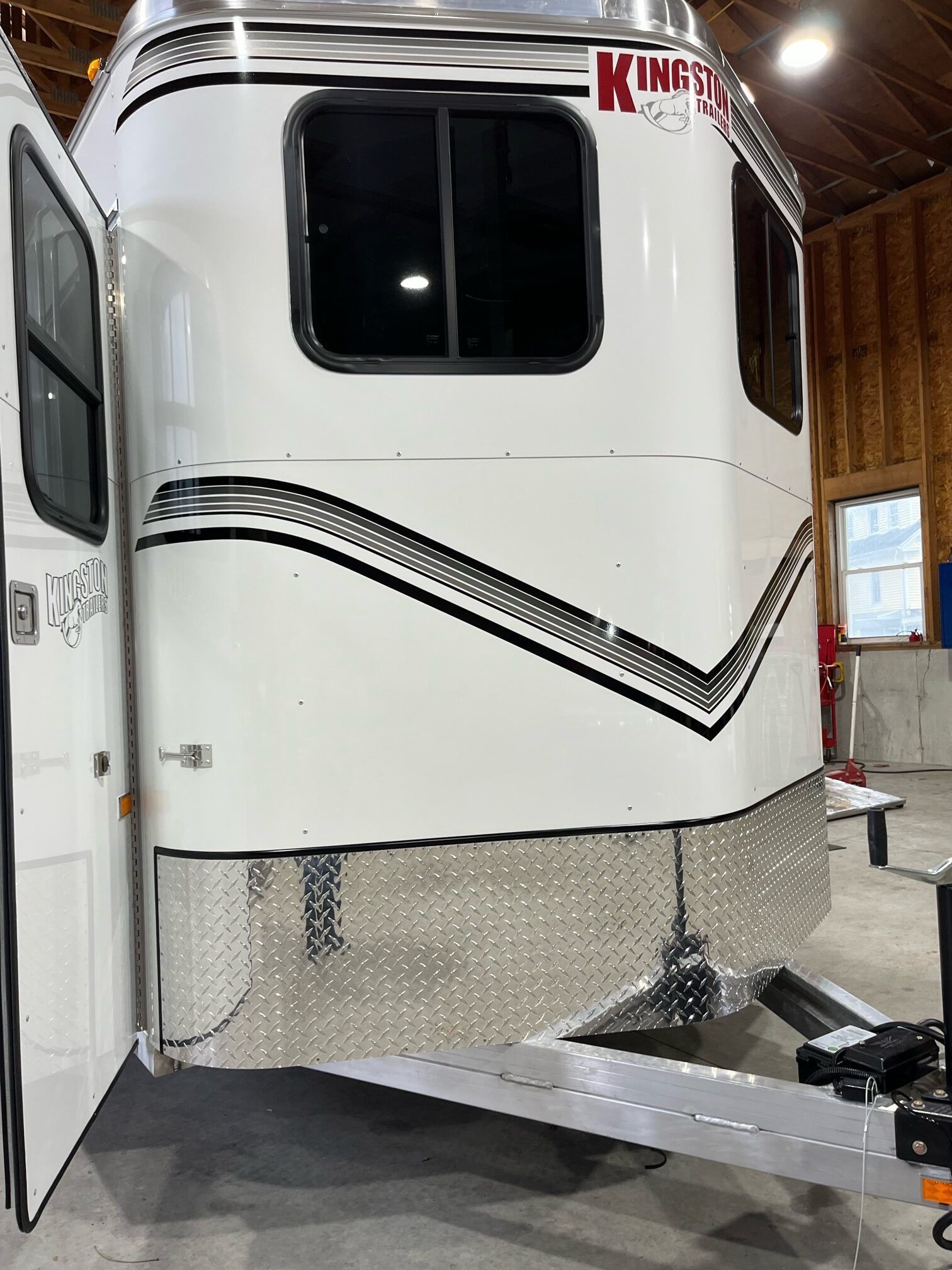 A white horse trailer is parked in a barn with the door open.