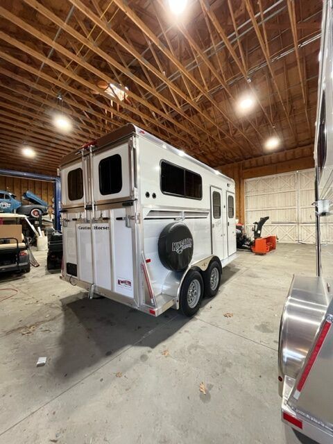 A horse trailer is parked in a garage next to a car.
