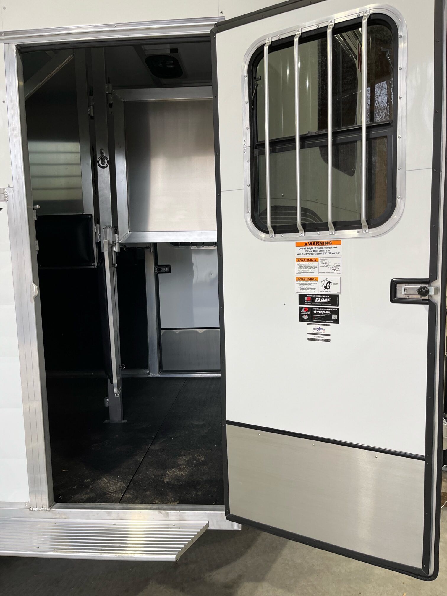 The door of a horse trailer is open and shows the inside of the trailer.
