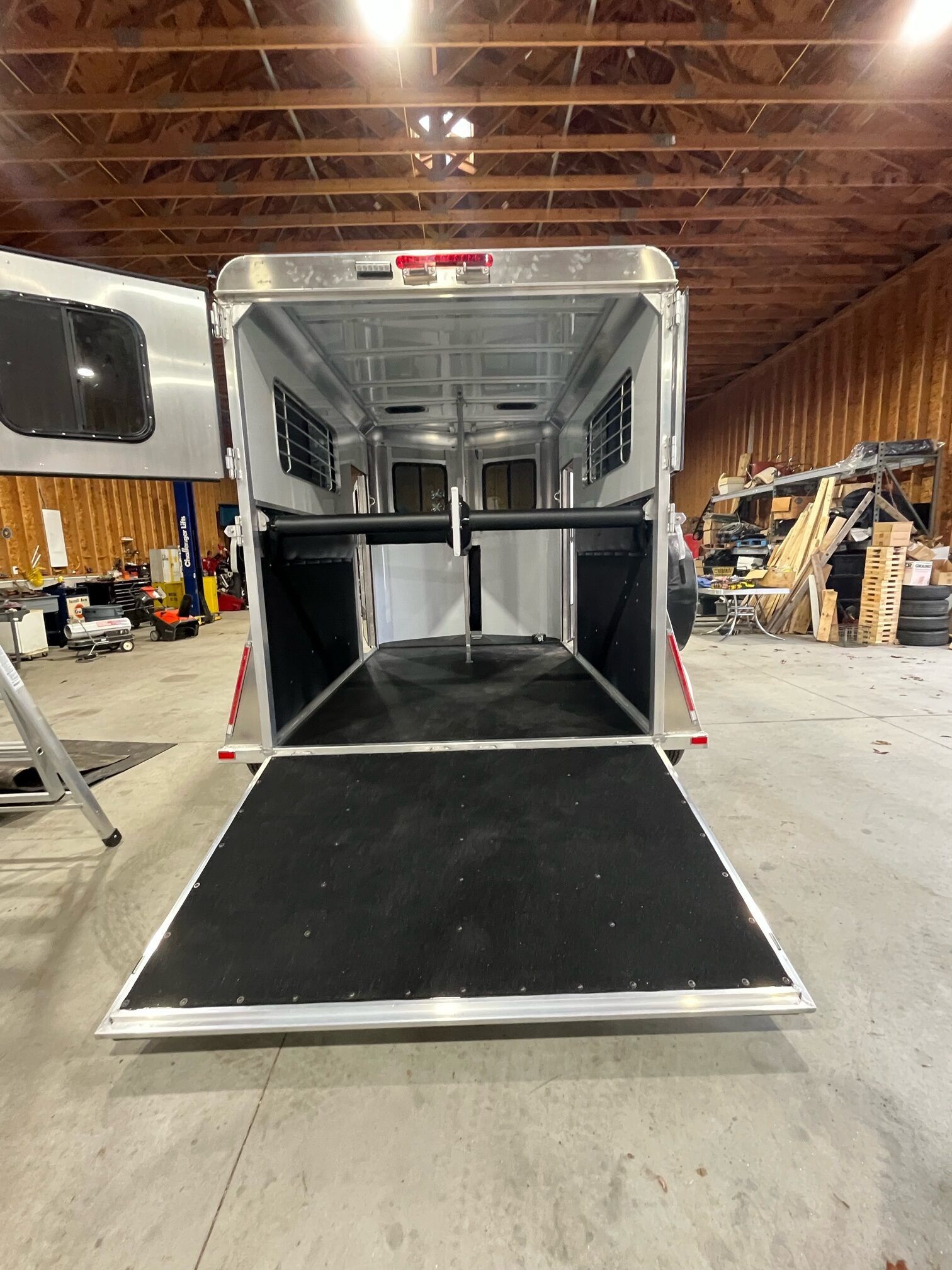 A horse trailer is sitting in a warehouse with the door open.