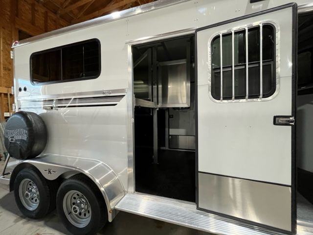 A horse trailer with the door open is parked in a garage.