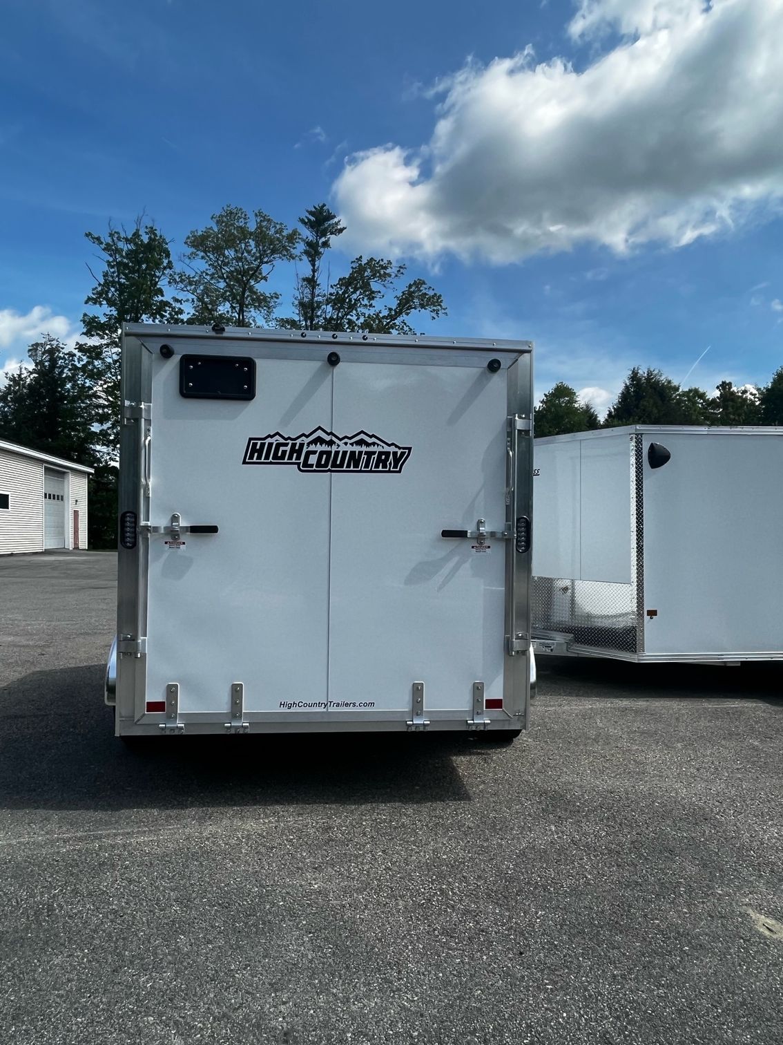 Two white trailers are parked next to each other in a parking lot.