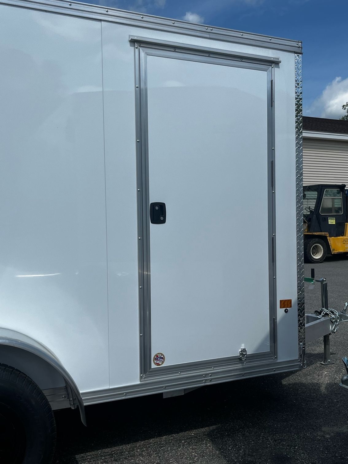 A white trailer is parked next to a yellow forklift