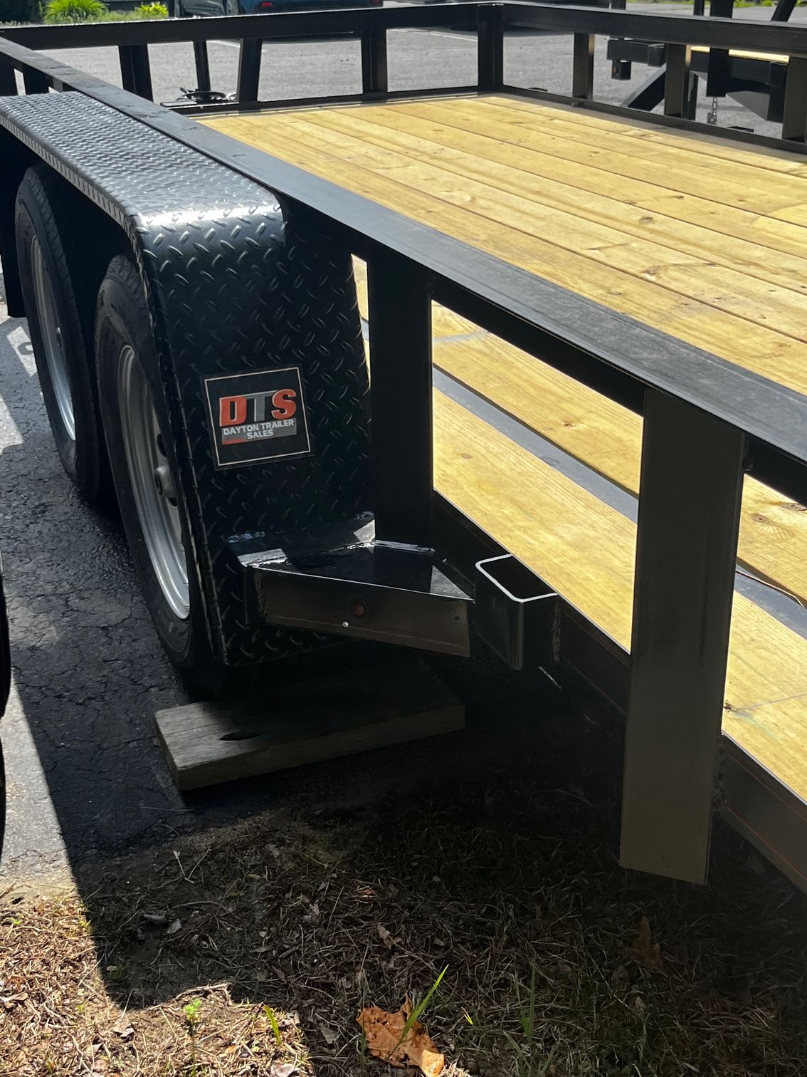 A trailer with a wooden deck is parked on the side of the road.