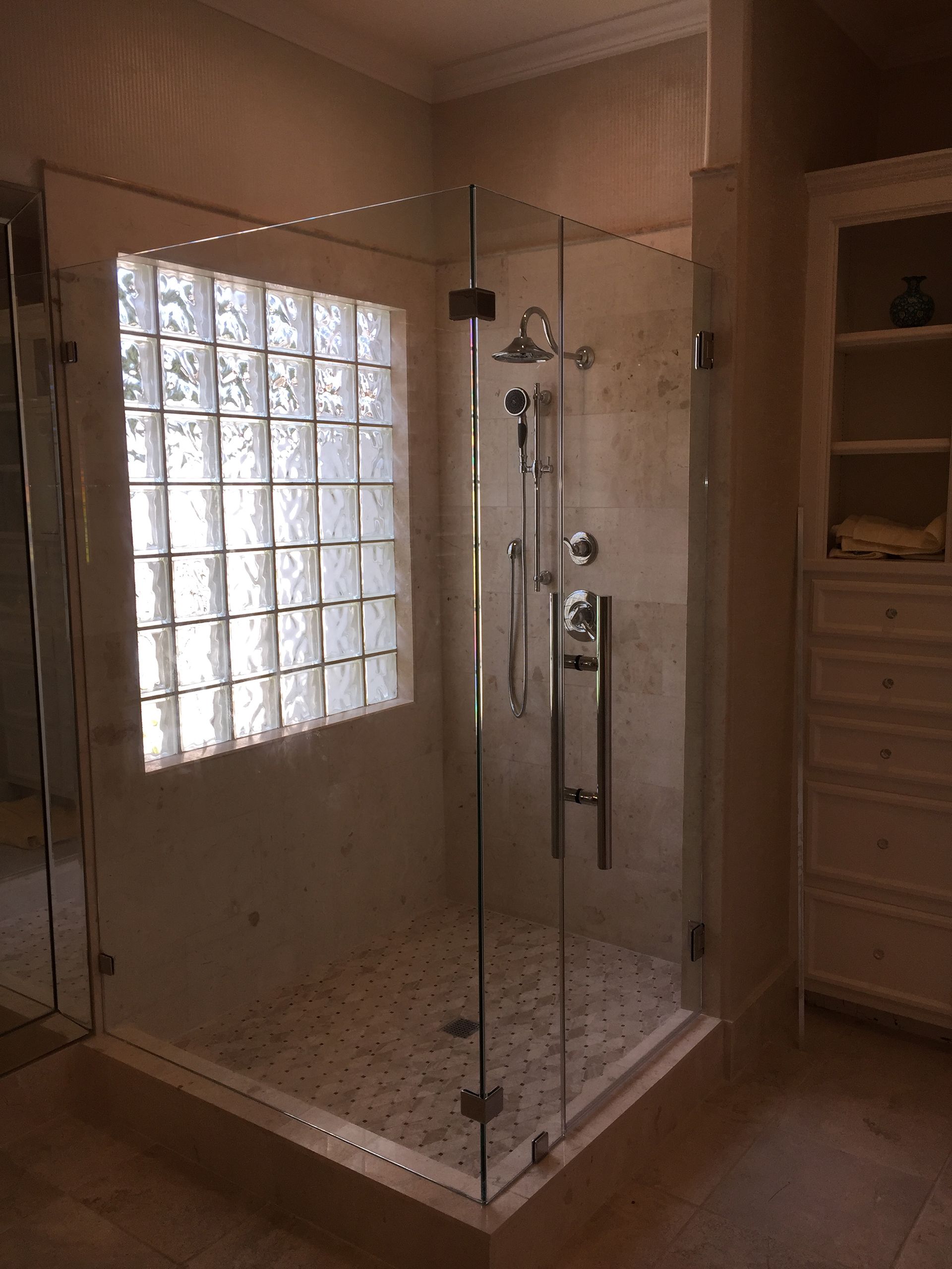 Glass-enclosed shower with glass block window, beige tile, and stainless steel fixtures in a bathroom.