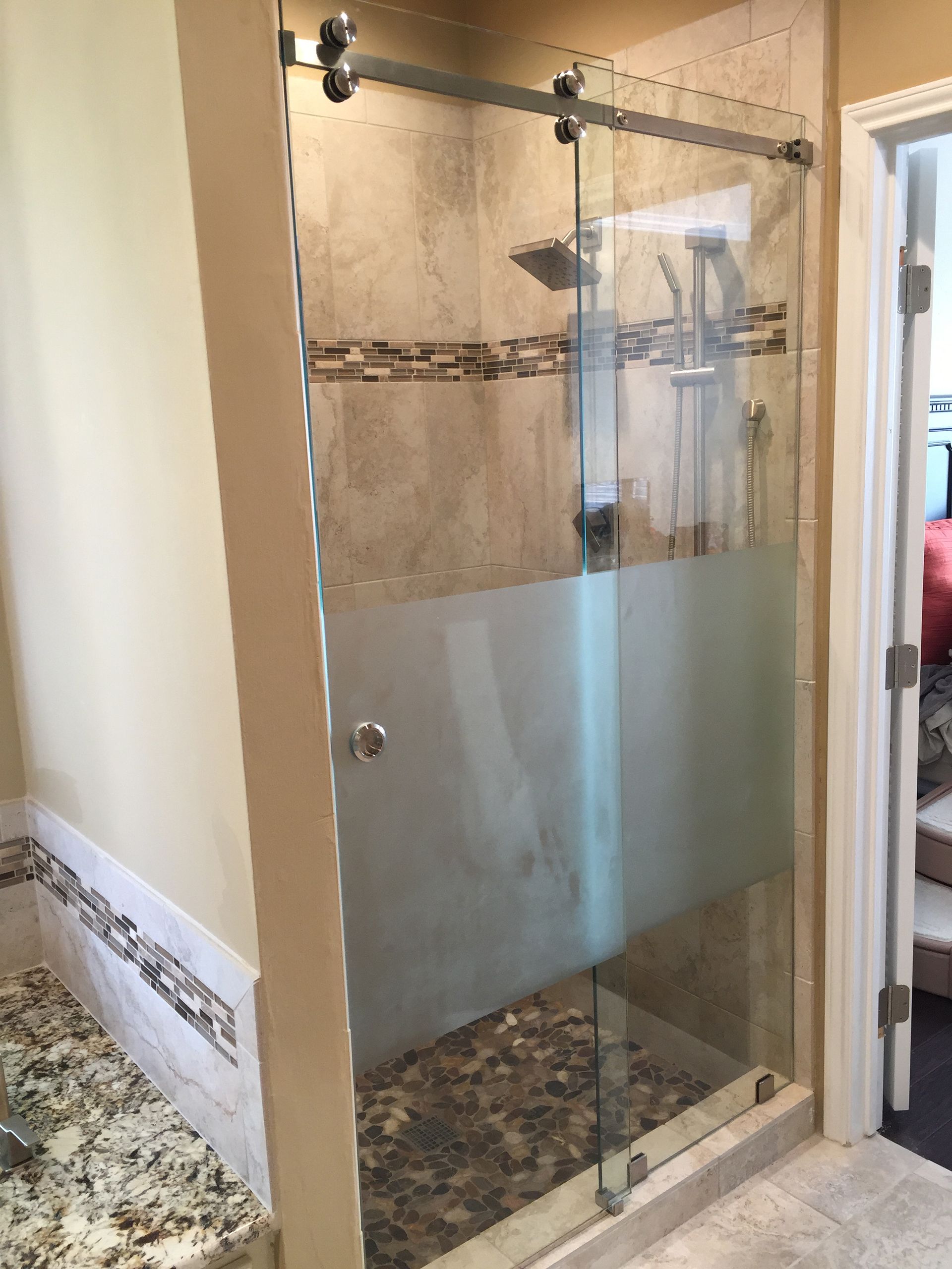 Glass shower door with frosted bottom panel, pebble floor, and beige tile.