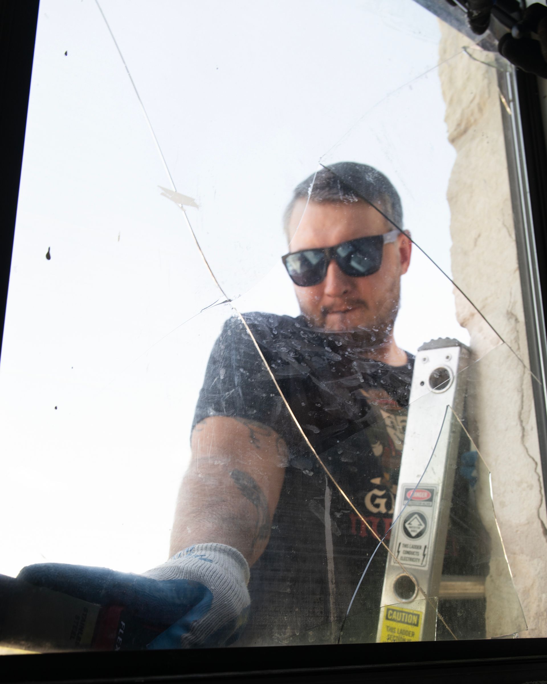 Man in sunglasses looking at cracked glass, holding a level.