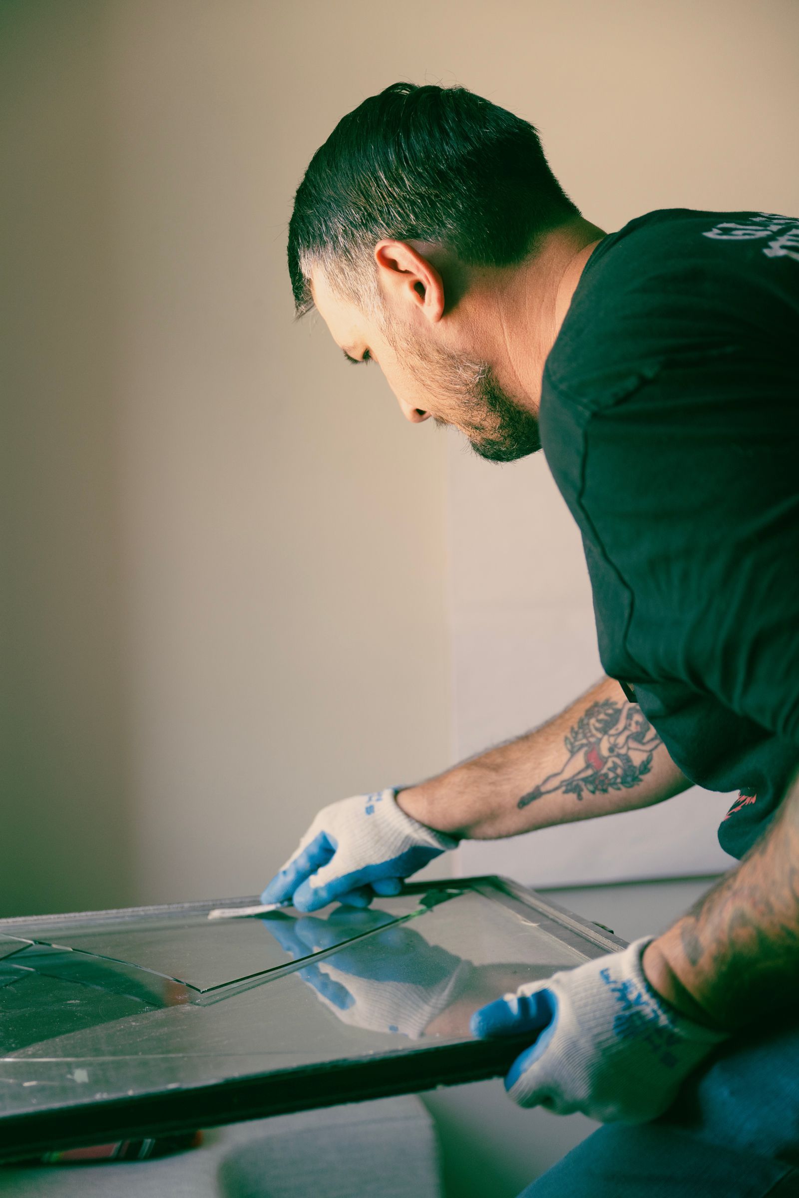 Man in gloves inspects a pane of glass. He’s in a room, holding the glass, looking down.