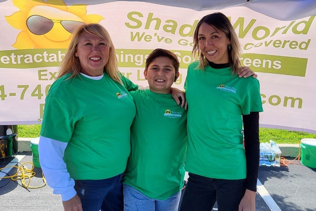 Three people are posing for a picture in front of a sign that says shade world.
