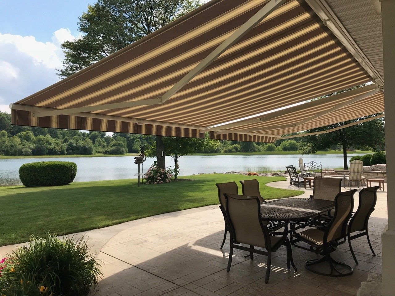 A patio with a table and chairs under an awning overlooking a lake