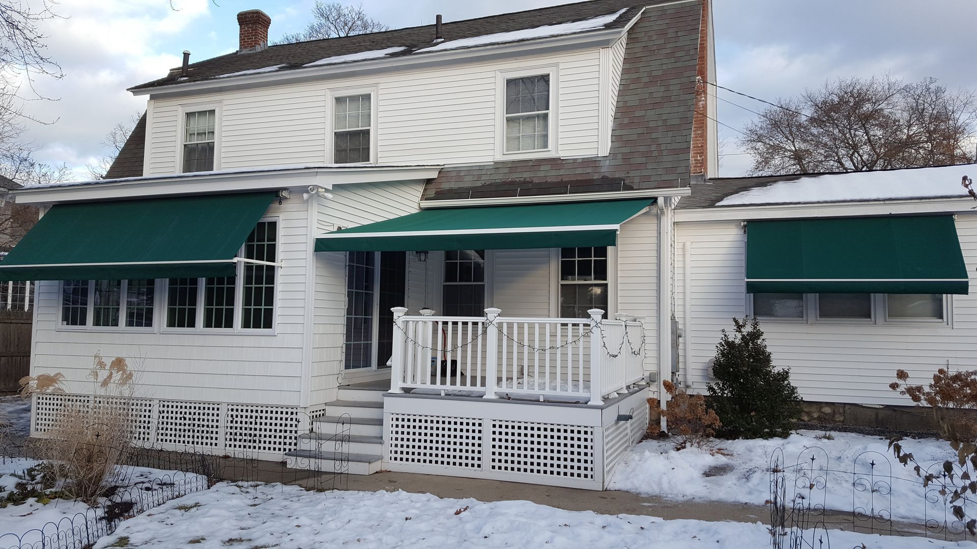 A white house with green awnings on the windows.