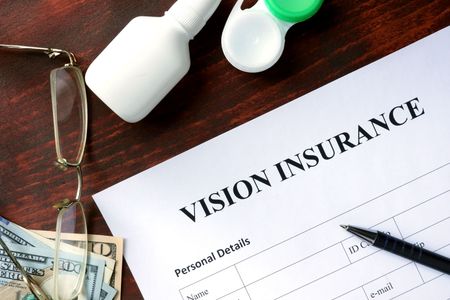 A vision insurance form on a table with glasses and contact lenses